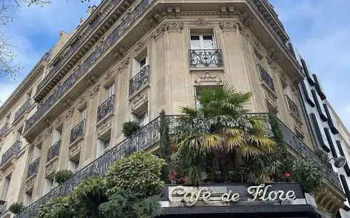 Café de Flore facade in Saint-Germain-des-Prés, Paris, with ornate balconies and greenery.