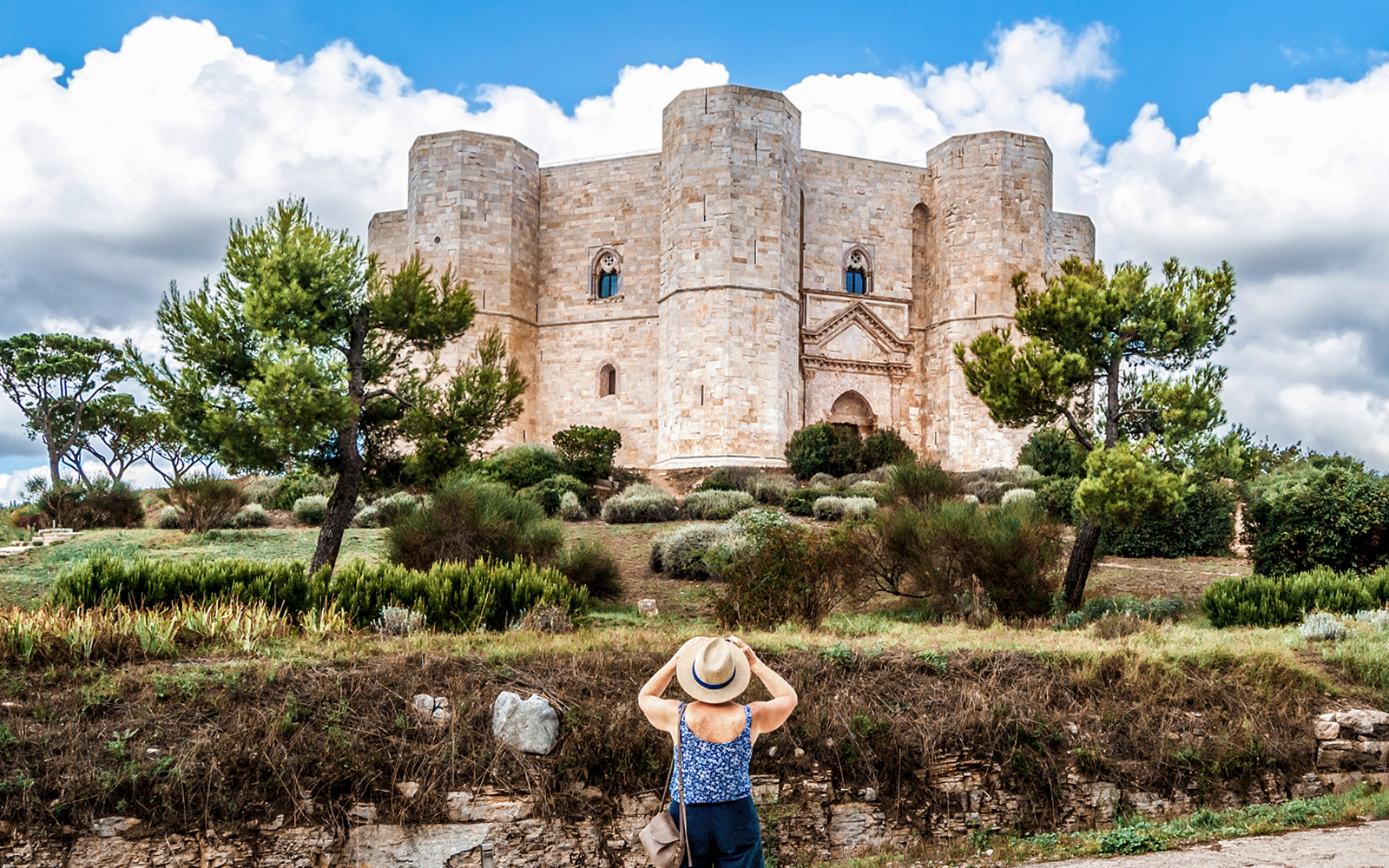 A women tourist with her traveller hat on, clicking a photo of the Castel from the outer area.
