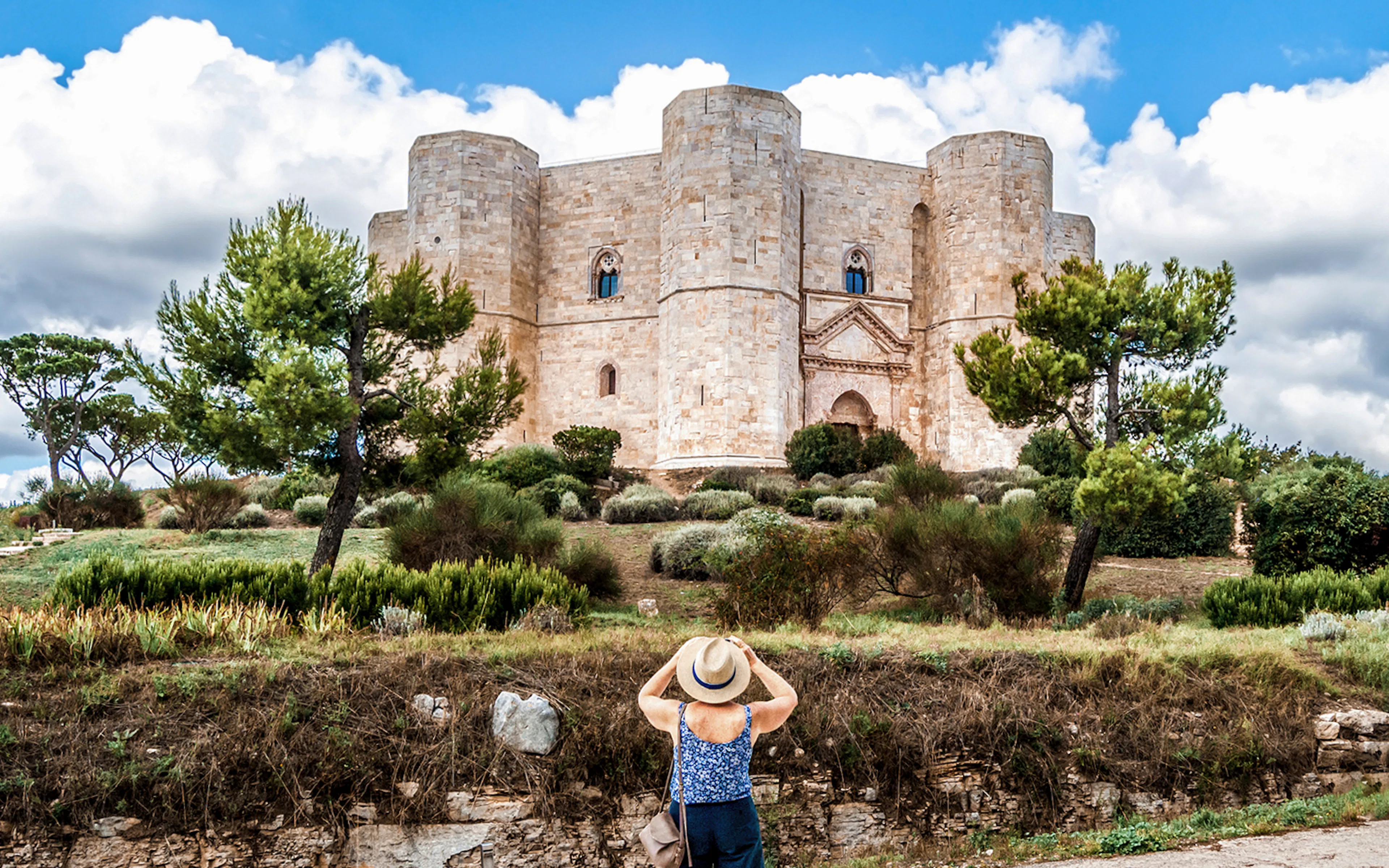 Visitor admiring Castel del Monte in Italy, surrounded by greenery.