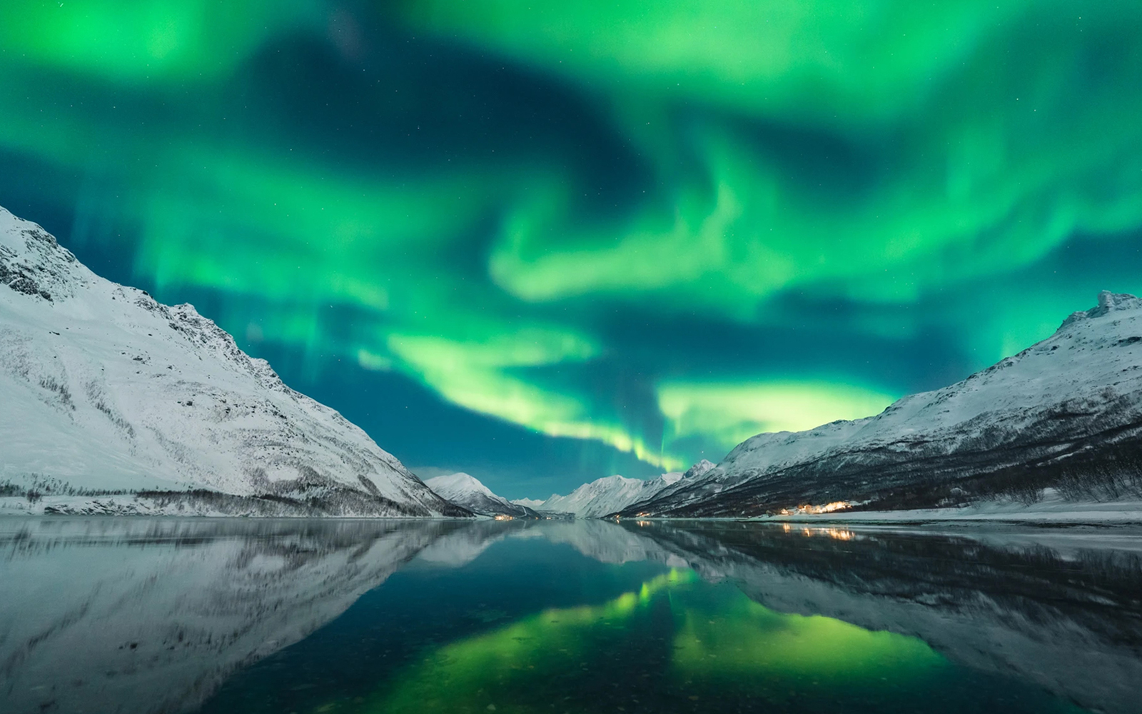 Northern lights over snowy mountains and a reflective lake during a chase tour.