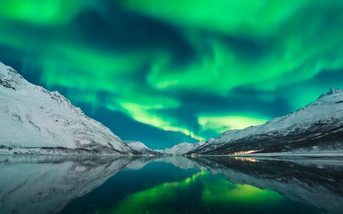 Northern lights over snowy mountains and a reflective lake during a chase tour.