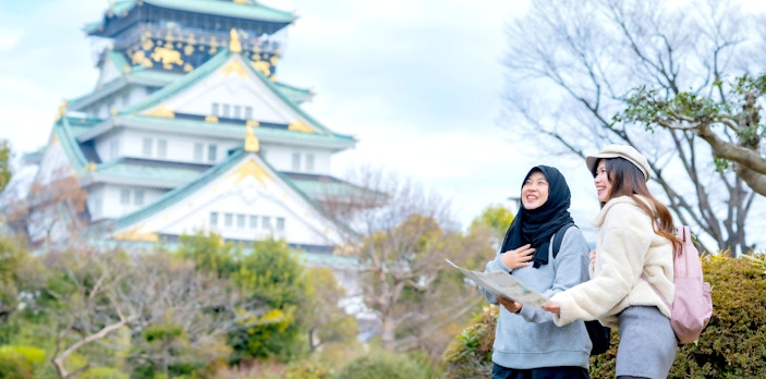 Two friends exploring Osaka Castle, Japan, with a map.