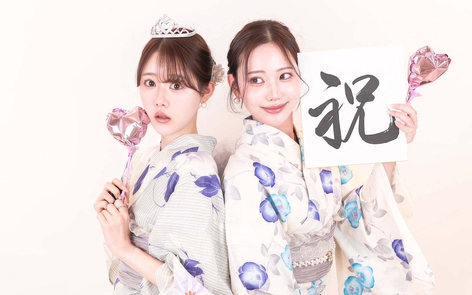Two people wearing yukata holding heart-shaped balloons and a calligraphy sign.