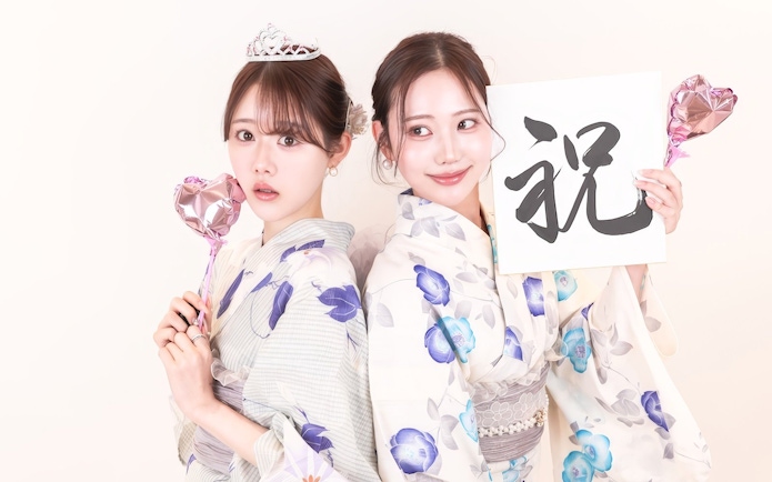 Two people wearing yukata holding heart-shaped balloons and a calligraphy sign.