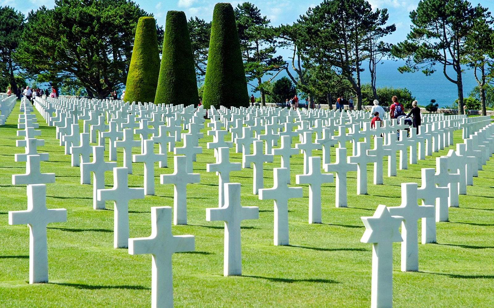 Visitors walking among white crosses at Normandy American Cemetery near Omaha Beach.