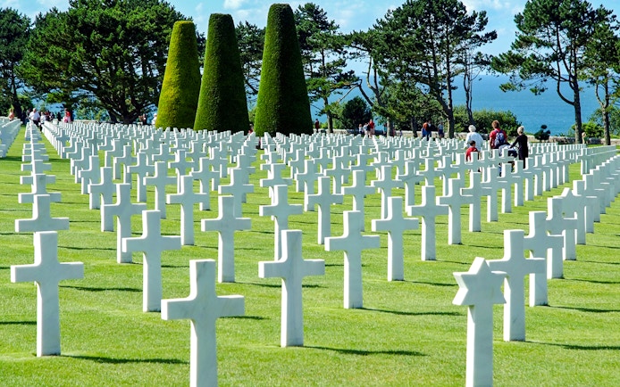 Visitors walking among white crosses at Normandy American Cemetery near Omaha Beach.