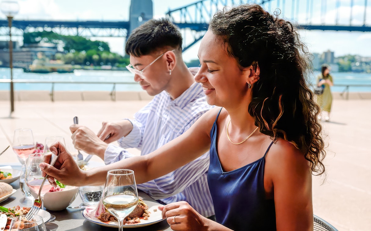 People dining at Midden by Mark Olive with Sydney Harbour Bridge in the background.