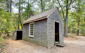 Replica of Thoreau's cabin at Walden Pond, Concord, MA, surrounded by trees.