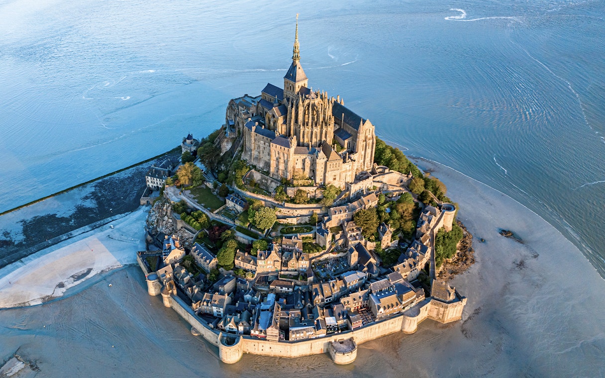 Aerial view of Mont Saint Michel surrounded by water and sand in Normandy, France.