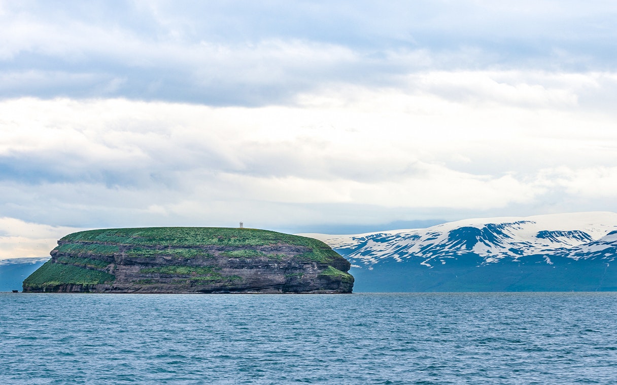 Lundey Island in Husavik, Iceland with ocean and snow-capped mountains in the background.
