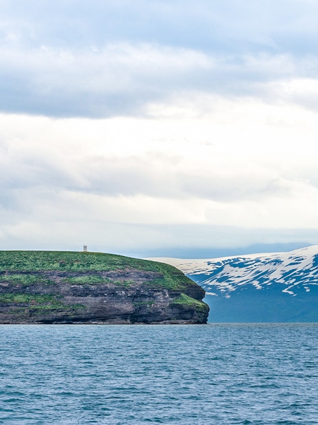 Lundey Island in Husavik, Iceland with ocean and snow-capped mountains in the background.