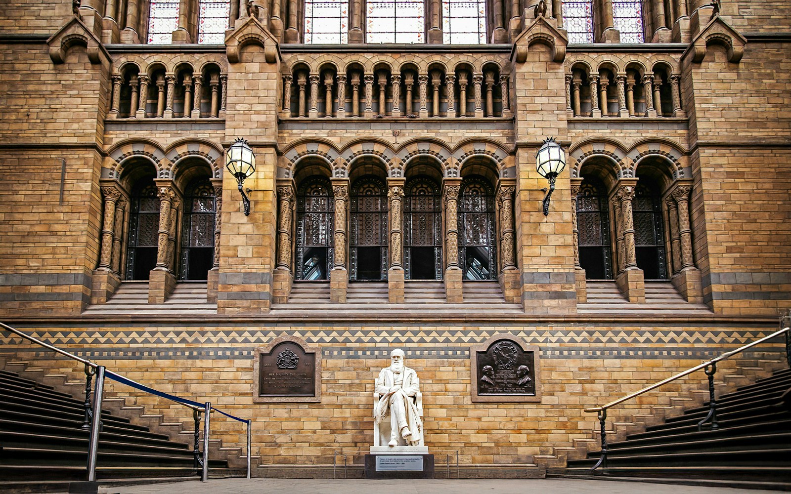 Charles Darwin statue inside Natural History Museum London with visitors exploring exhibits.