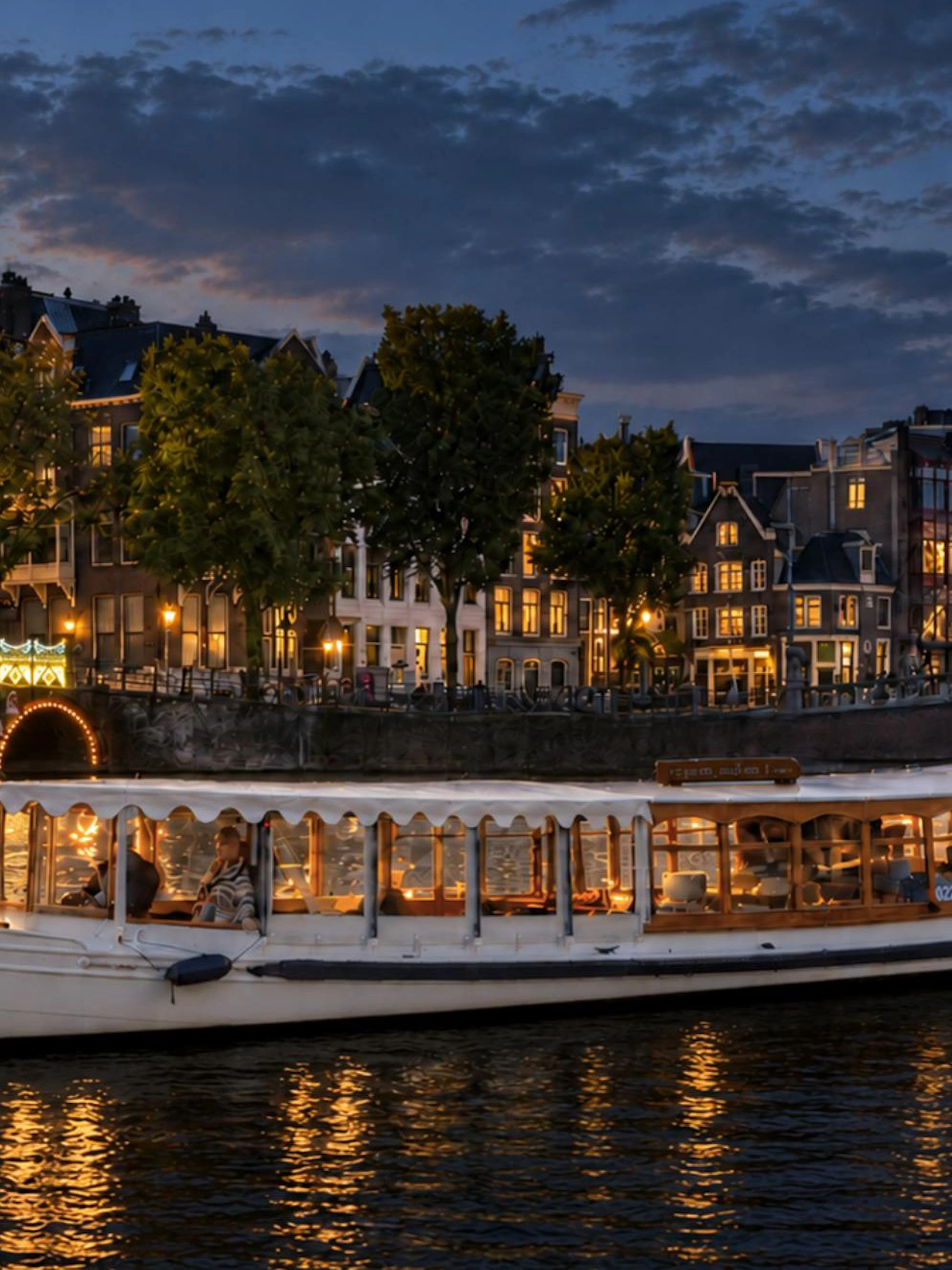 Canal boat cruising during Amsterdam Light Festival with illuminated bridge and historic buildings.