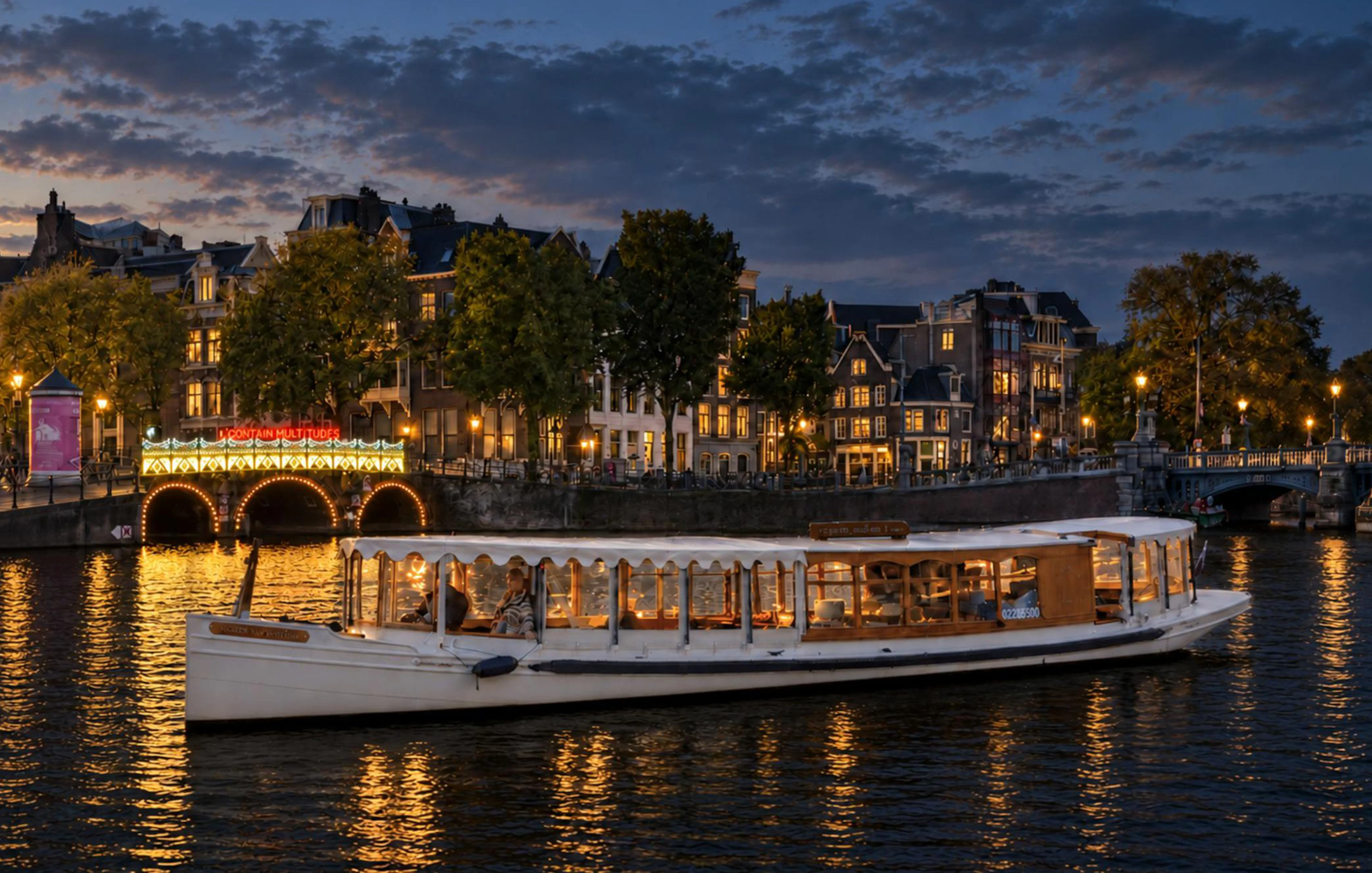 Canal boat cruising during Amsterdam Light Festival with illuminated bridge and historic buildings.