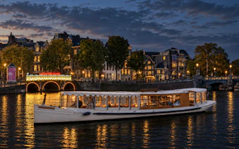 Canal boat cruising during Amsterdam Light Festival with illuminated bridge and historic buildings.