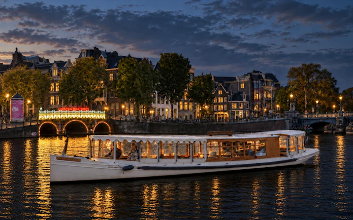 Canal boat cruising during Amsterdam Light Festival with illuminated bridge and historic buildings.