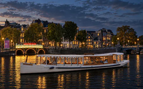 Canal boat cruising during Amsterdam Light Festival with illuminated bridge and historic buildings.