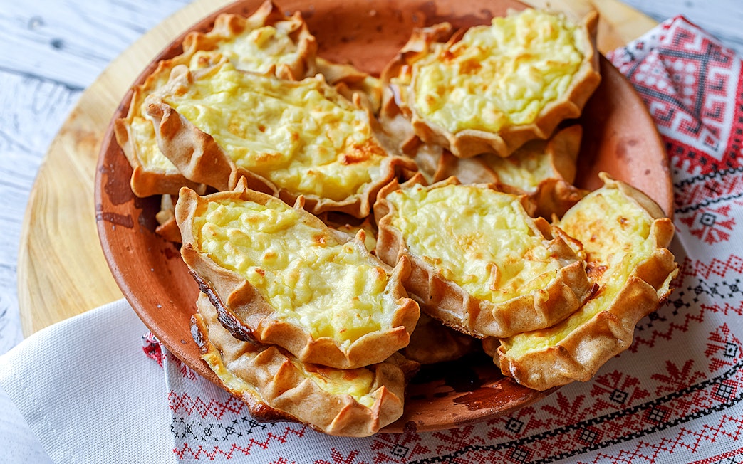 Traditional Finnish Karelian pies on a wooden plate, served on a patterned cloth.