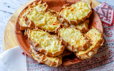 Traditional Finnish Karelian pies on a wooden plate, served on a patterned cloth.