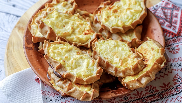 Traditional Finnish Karelian pies on a wooden plate, served on a patterned cloth.