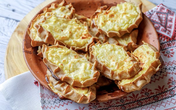 Traditional Finnish Karelian pies on a wooden plate, served on a patterned cloth.