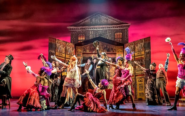 Stage performance of "My Fair Lady" with actors in vibrant costumes and a lively backdrop.
