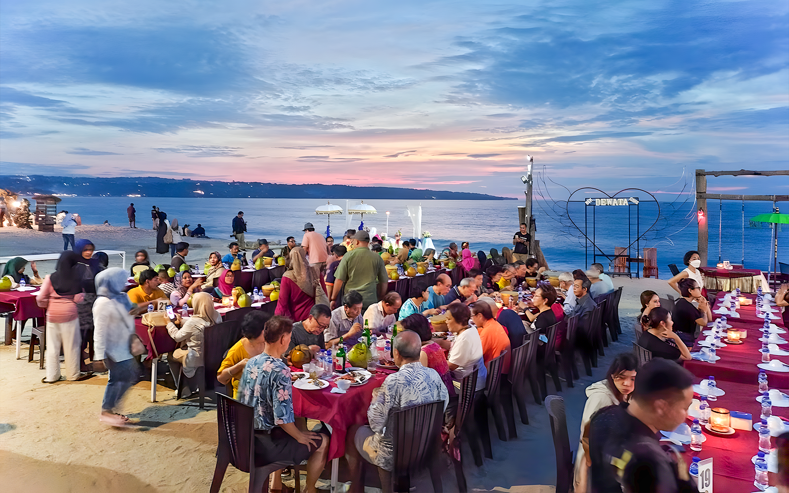 Group dining at sunset on Jimbaran Beach, Bali, with seafood and ocean view.