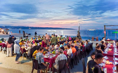 Group dining at sunset on Jimbaran Beach, Bali, with seafood and ocean view.