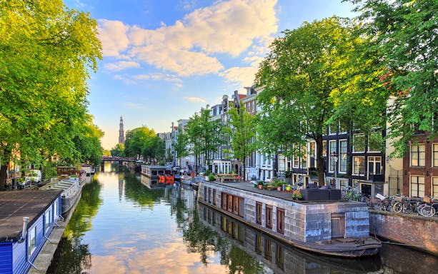 Amsterdam canal with houseboats and historic buildings under a blue sky.