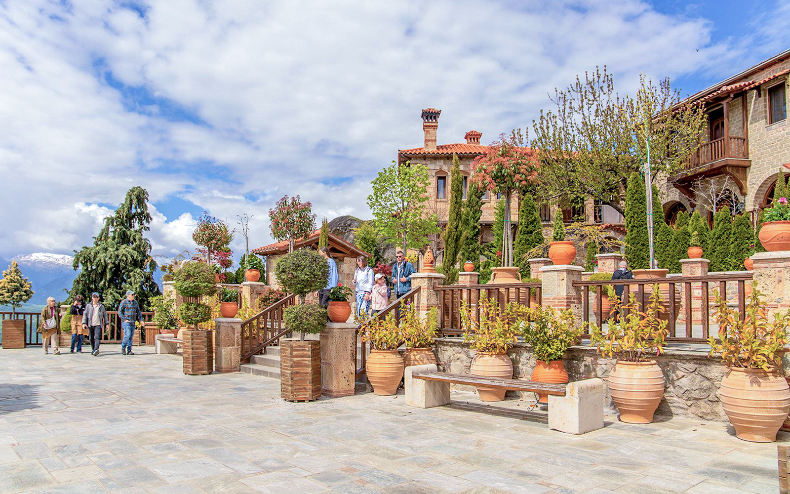 Meteora monastery courtyard with visitors, surrounded by potted plants and stone architecture.