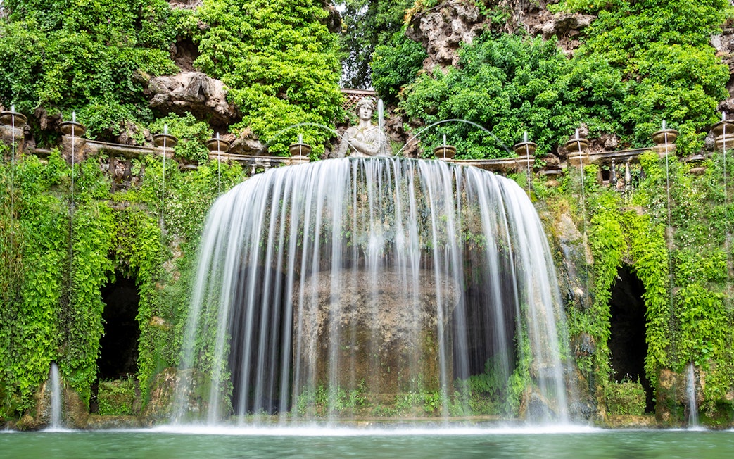 Villa d’Este waterfall with lush greenery and classical statue in Tivoli, Italy.
