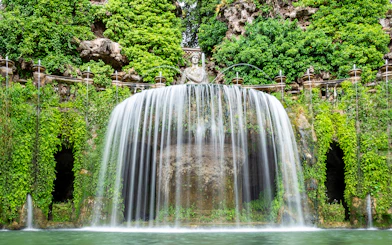Villa d’Este waterfall with lush greenery and classical statue in Tivoli, Italy.