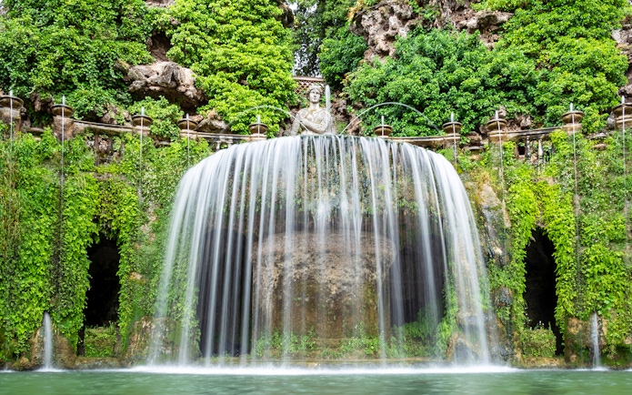 Villa d’Este waterfall with lush greenery and classical statue in Tivoli, Italy.