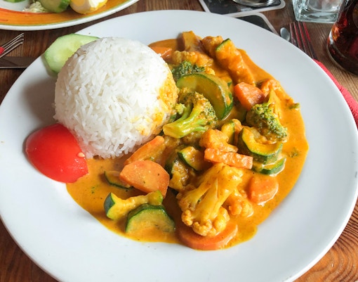 Seafood rice dish with vegetables and curry sauce on a white plate.