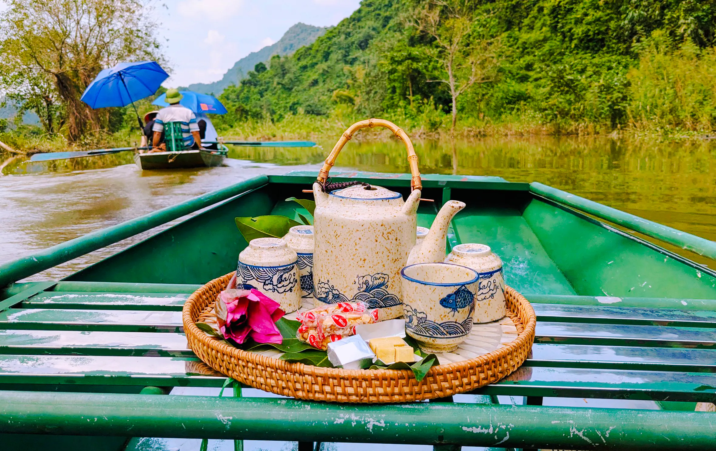 Ceramic tea set on a boat in Tam Coc, Ninh Binh, with lush greenery and river view.