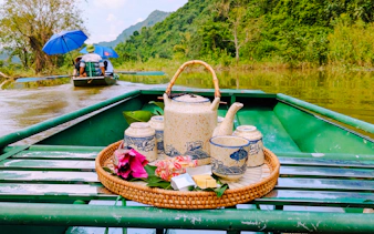 Ceramic tea set on a boat in Tam Coc, Ninh Binh, with lush greenery and river view.