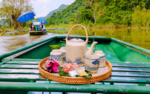 Ceramic tea set on a boat in Tam Coc, Ninh Binh, with lush greenery and river view.