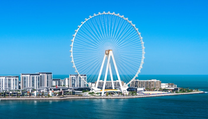 Ain Dubai Ferris wheel against a clear blue sky and ocean.