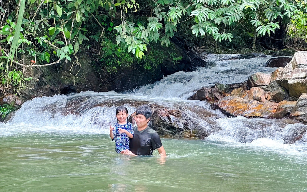 Father and daughter enjoying a waterfall in a lush forest setting.