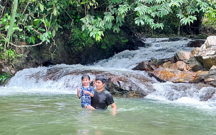 Father and daughter enjoying a waterfall in a lush forest setting.