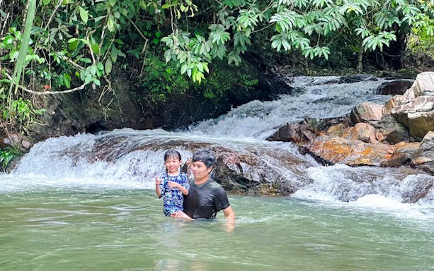 Father and daughter enjoying a waterfall in a lush forest setting.