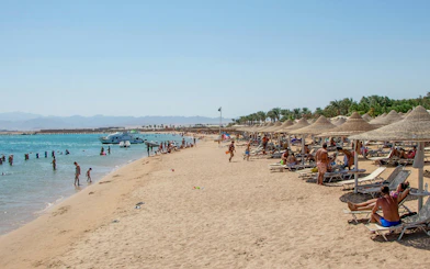 Beachgoers relaxing and swimming at Orange Bay Island, Hurghada, Egypt, with boats in the Red Sea.