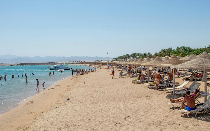 Beachgoers relaxing and swimming at Orange Bay Island, Hurghada, Egypt, with boats in the Red Sea.