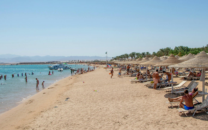 Beachgoers relaxing and swimming at Orange Bay Island, Hurghada, Egypt, with boats in the Red Sea.