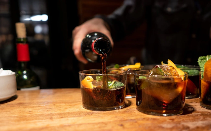 Pouring red wine into glasses with orange slices on a Barcelona tapas tour.