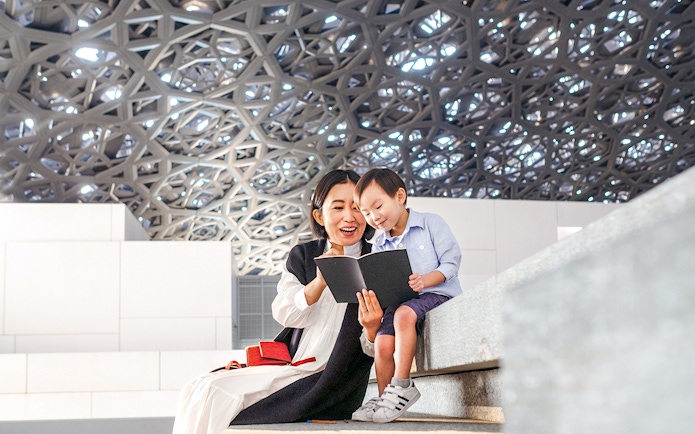 Guests reading a book under the dome at Louvre Museum Abu Dhabi.