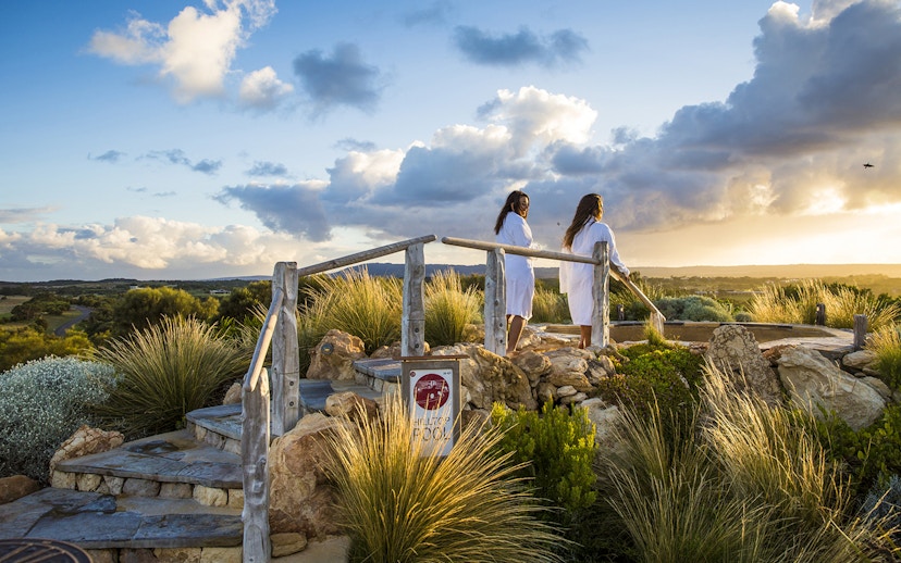 Visitors in robes at Peninsula Hot Springs overlook scenic landscape at sunrise.