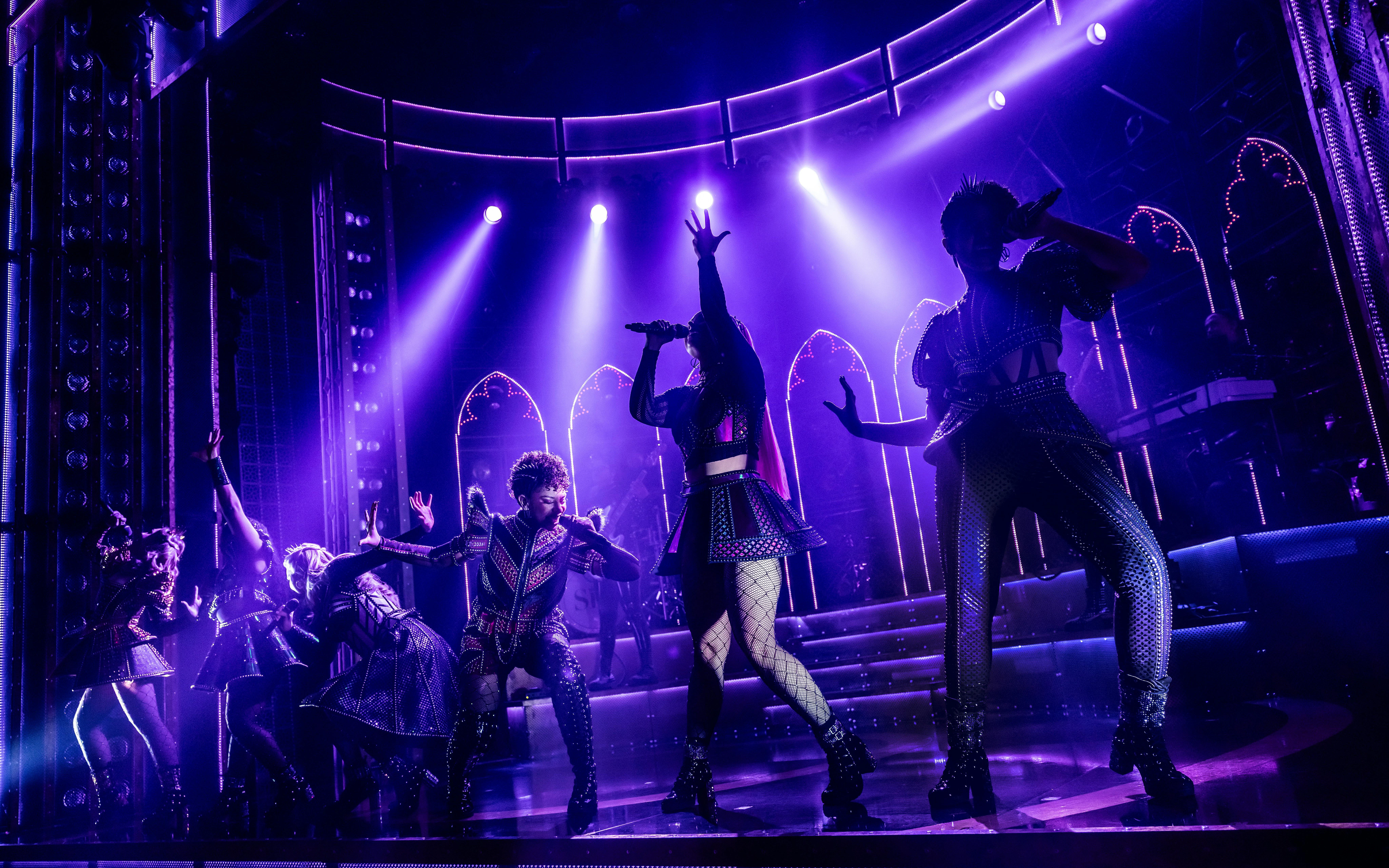 Performers on stage during Six musical at West End, vibrant lighting and dynamic poses.