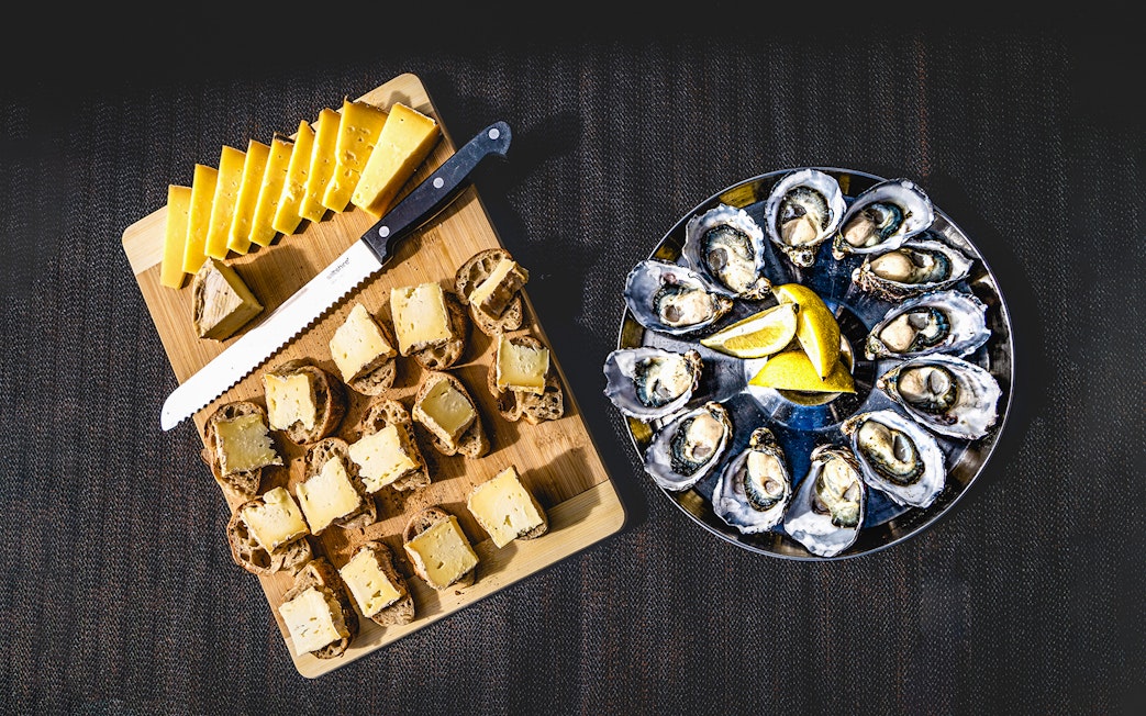 Bread with cheese and oysters served with lemon slices on a platter.