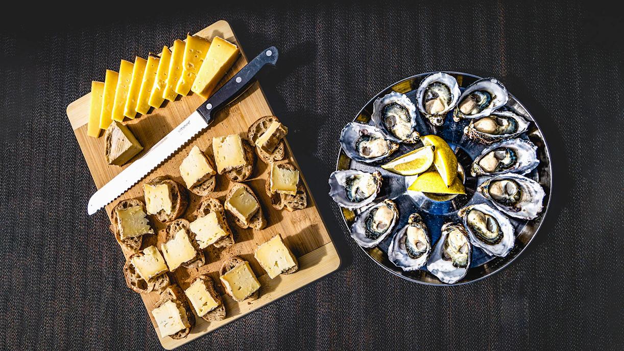 Bread with cheese and oysters served with lemon slices on a platter.